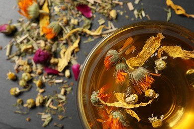 Photo of Freshly brewed tea and dried herbs on black table, top view