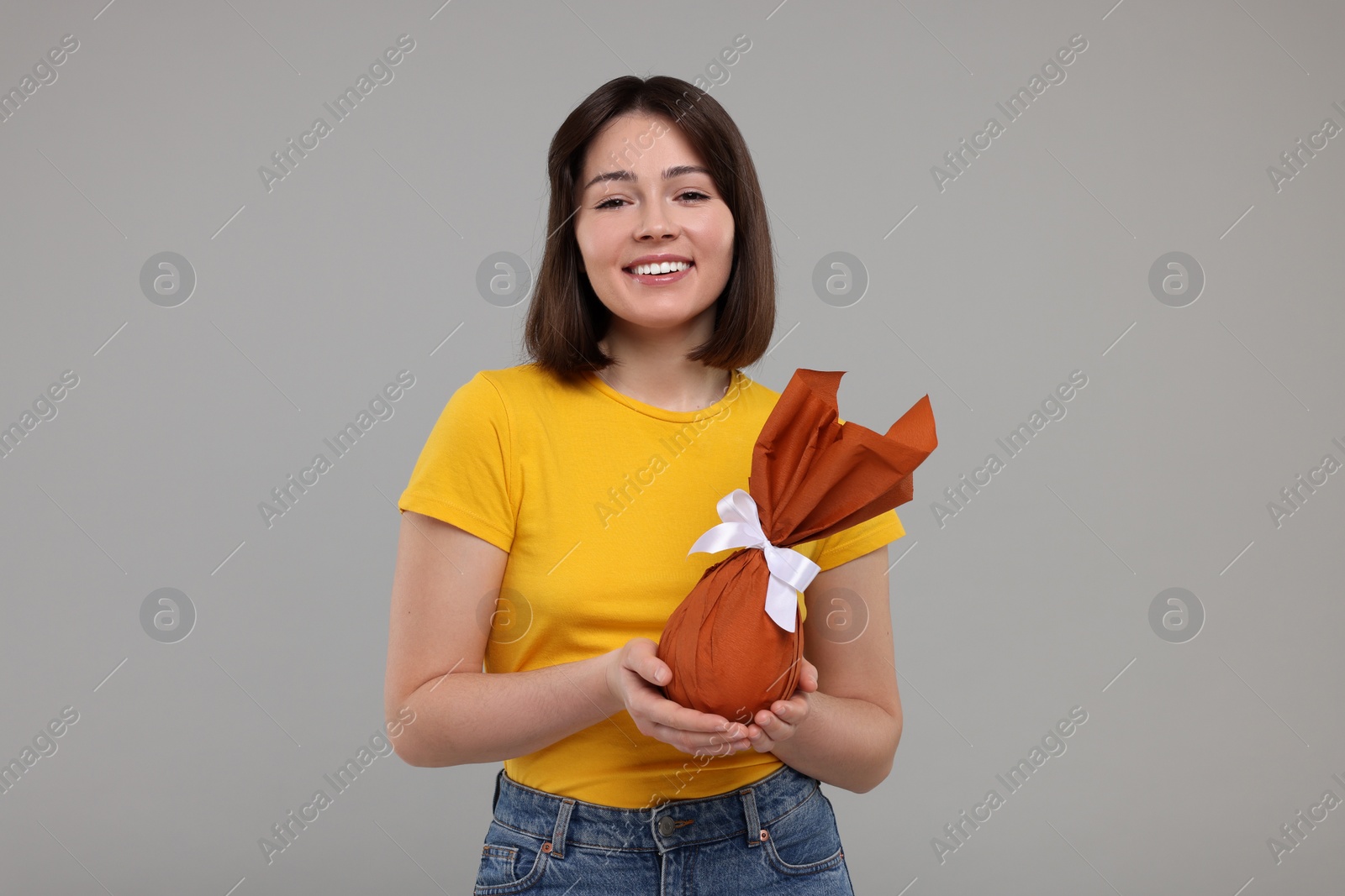 Photo of Easter celebration. Happy woman with wrapped egg on grey background