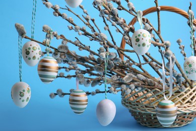 Photo of Wicker basket with beautiful willow branches and painted eggs on light blue background, closeup. Easter decor