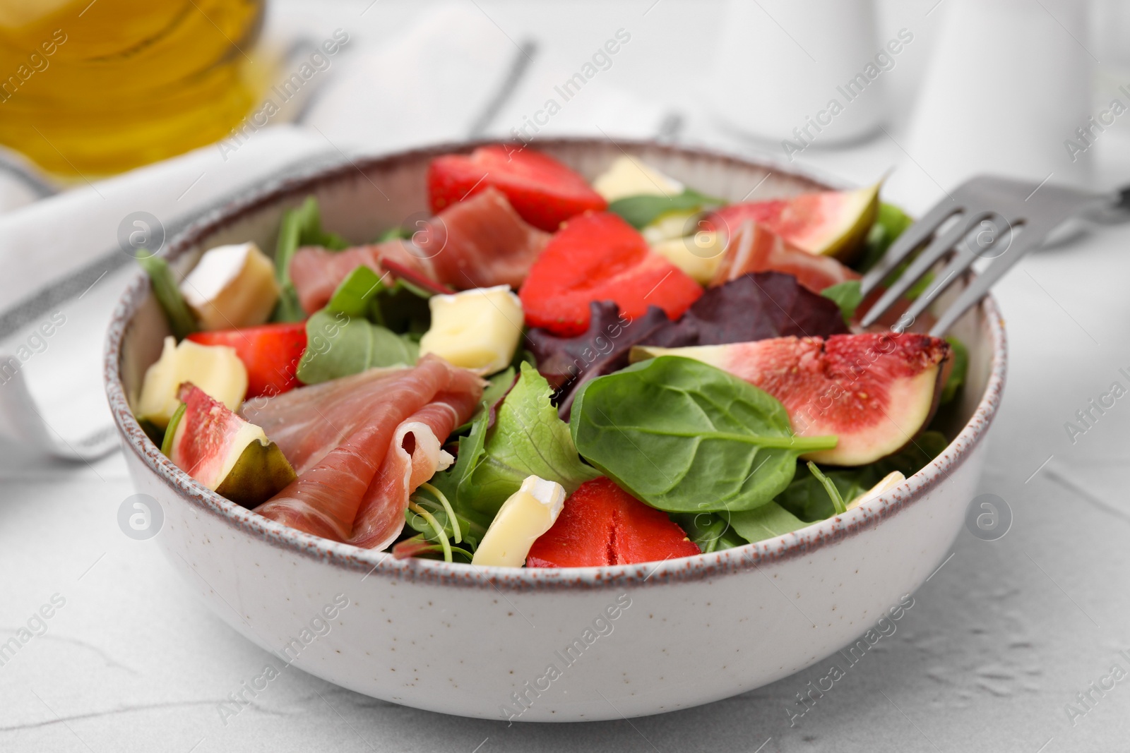 Photo of Tasty salad with brie cheese, prosciutto, strawberries and figs on white table, closeup