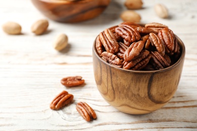 Photo of Tasty pecan nuts in dish on wooden table. Space for text