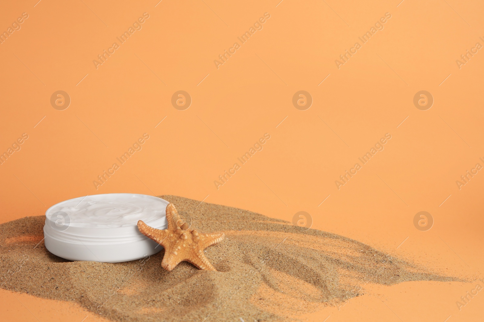 Photo of Jar with cream and starfish on sand against orange background, space for text. Cosmetic product