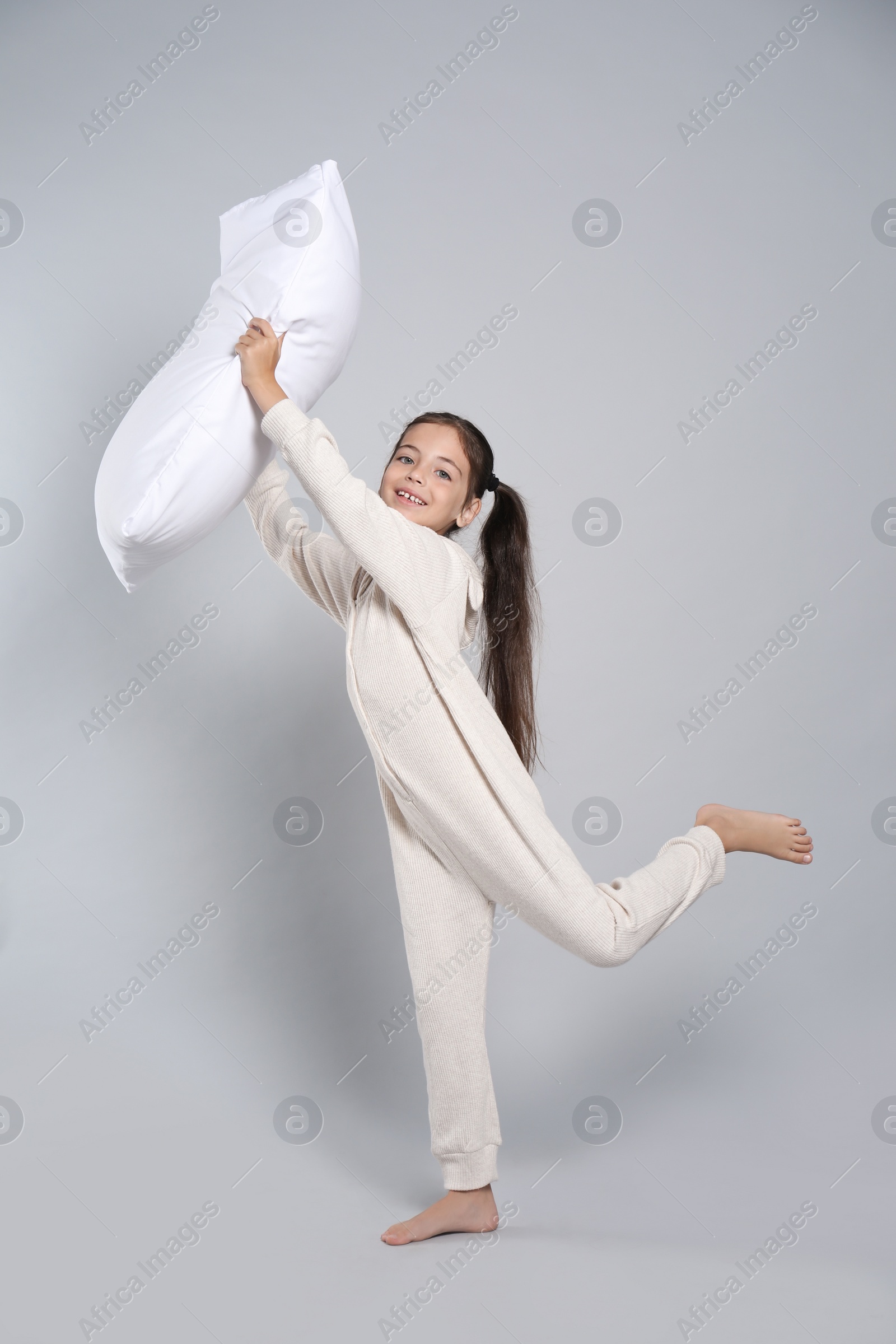 Photo of Cute girl in white pajamas with pillow on light grey background