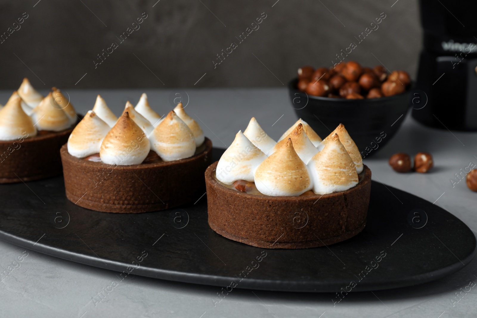 Photo of Delicious salted caramel chocolate tarts with meringue served on grey table, closeup