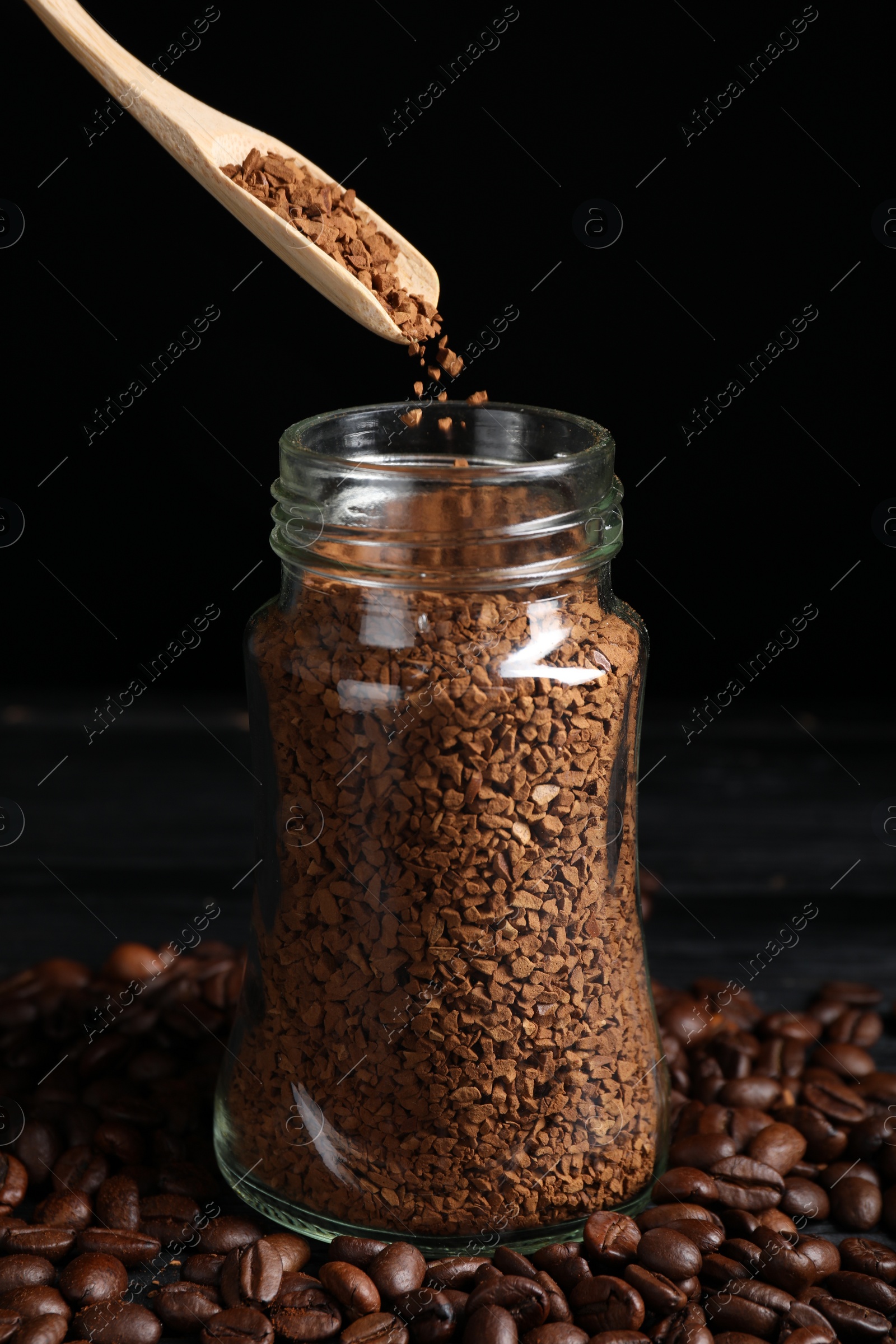 Photo of Putting instant coffee into glass jar on black wooden table