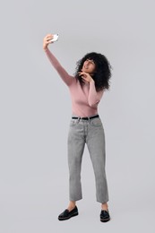 Beautiful young woman taking selfie on light grey background