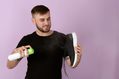 Young man spraying air freshener on shoe against color background