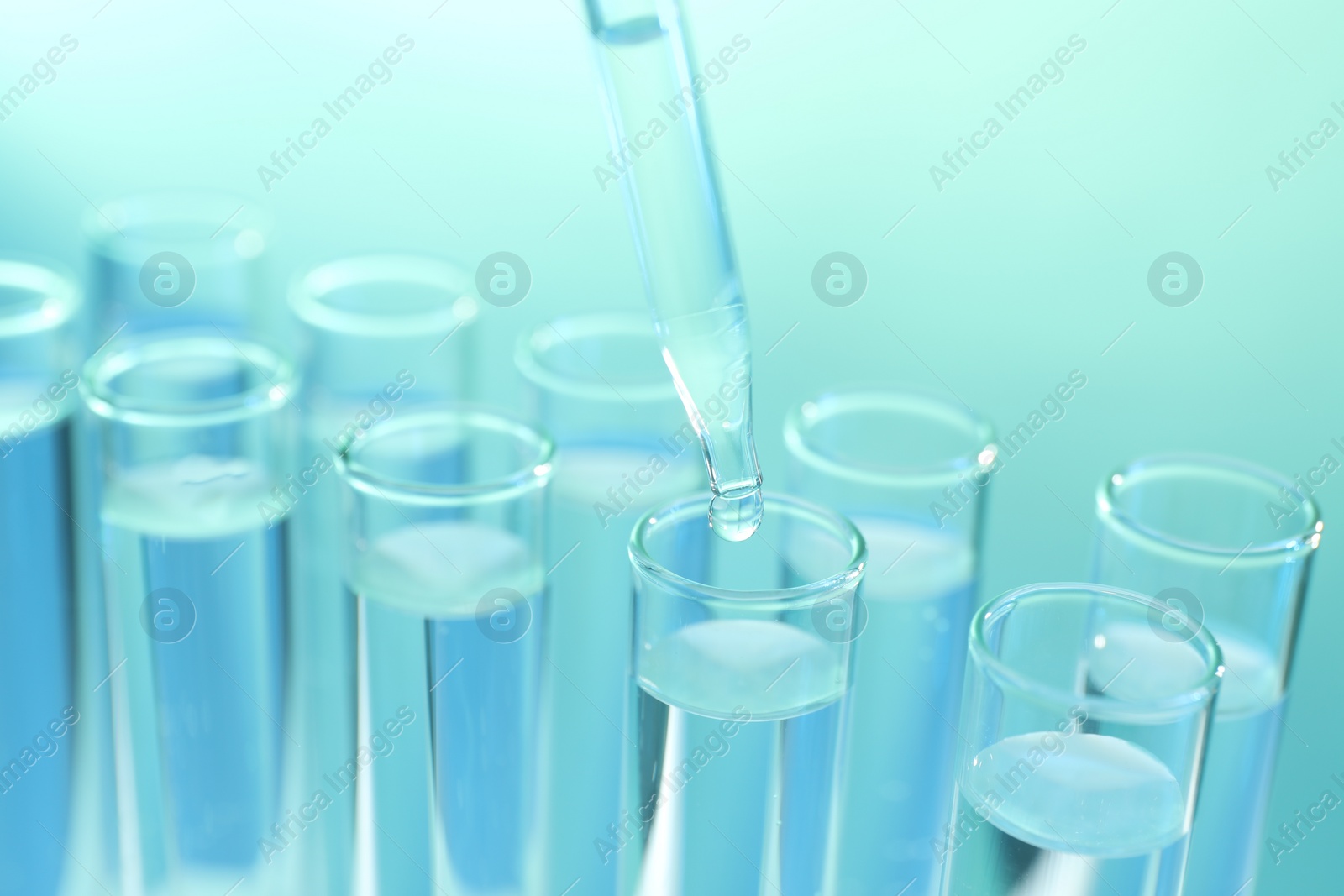 Photo of Dripping liquid from pipette into test tube on turquoise background, closeup