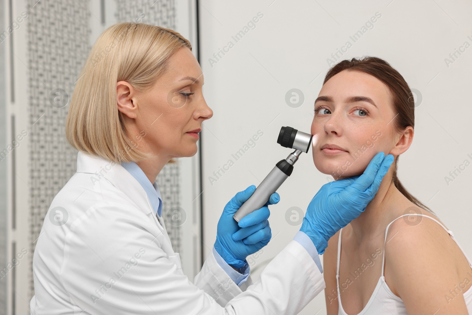 Photo of Dermatologist with dermatoscope examining patient`s face in clinic