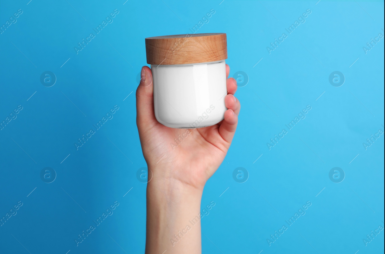 Photo of Woman holding jar of face cream on light blue background, closeup