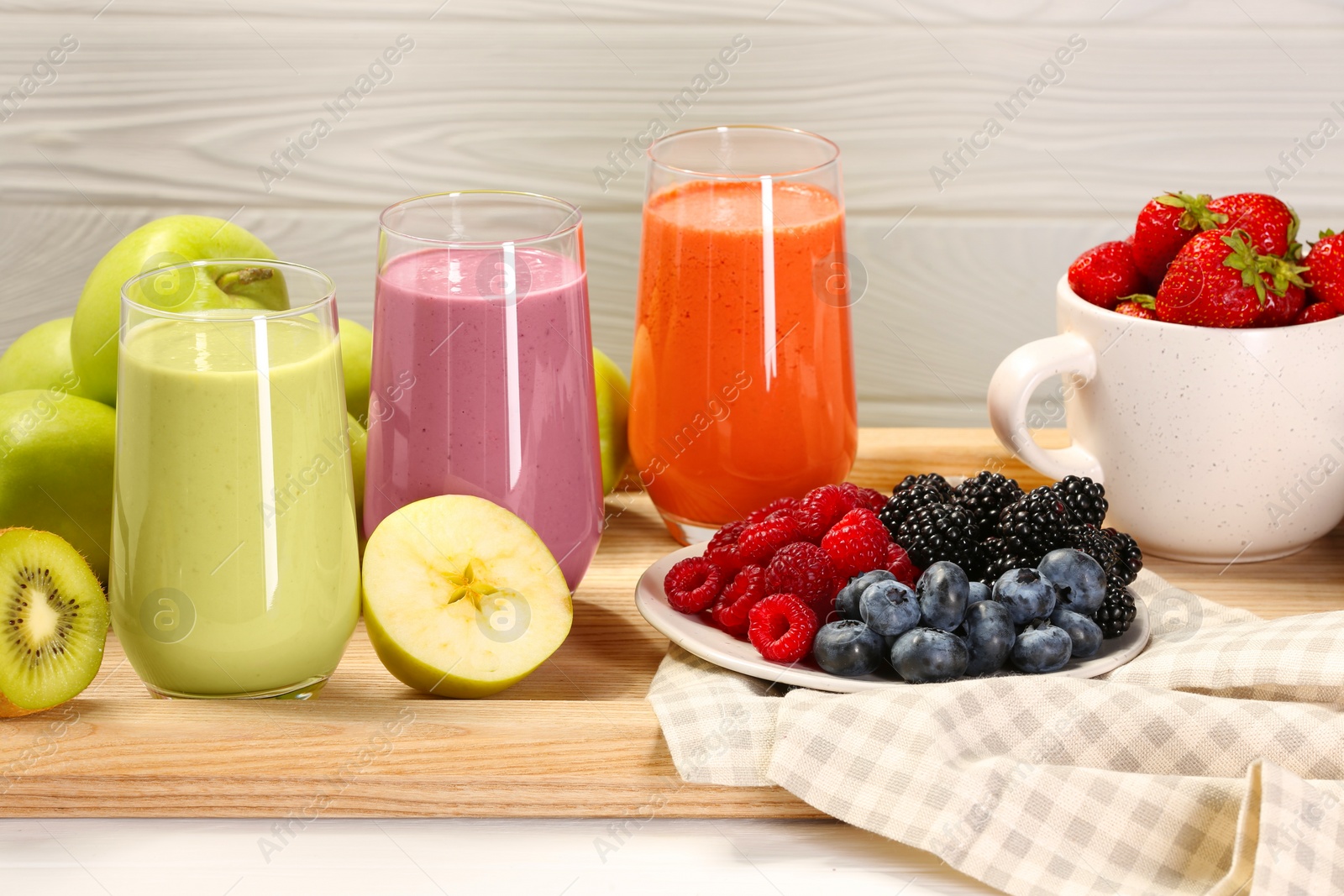 Photo of Glasses of different tasty smoothies and fresh ingredients on white wooden table