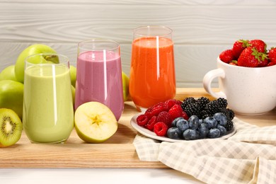 Photo of Glasses of different tasty smoothies and fresh ingredients on white wooden table