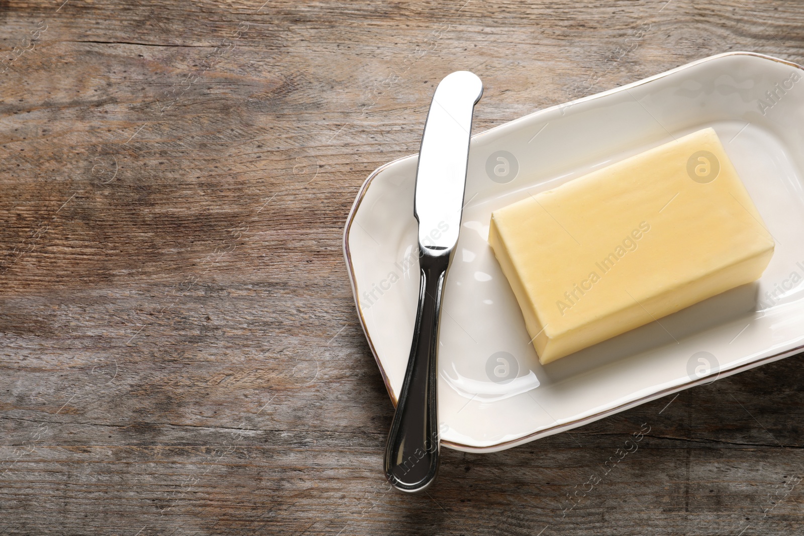 Photo of Dish with fresh butter and knife on wooden table. Space for text