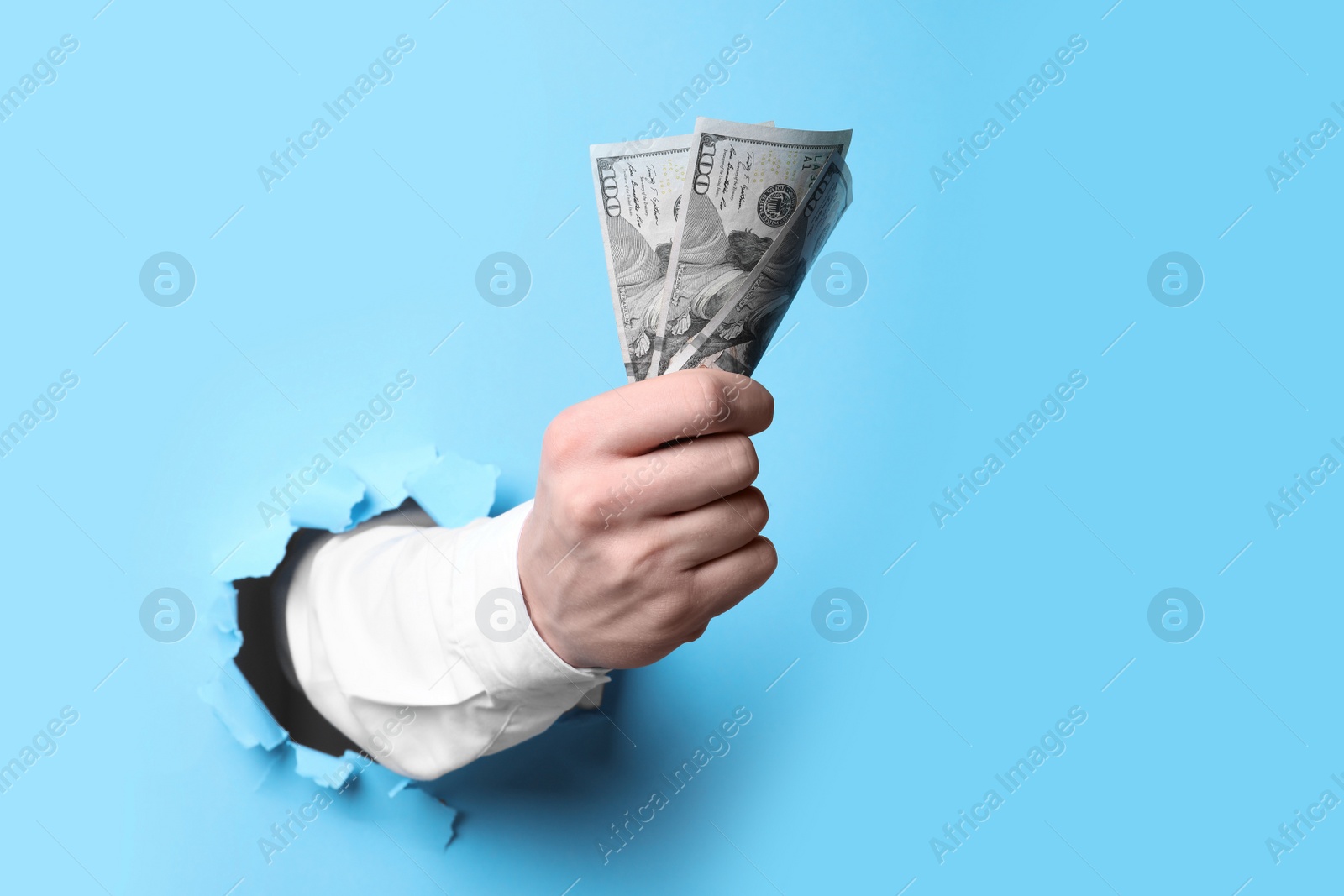 Photo of Businessman breaking through light blue paper with money in fist, closeup