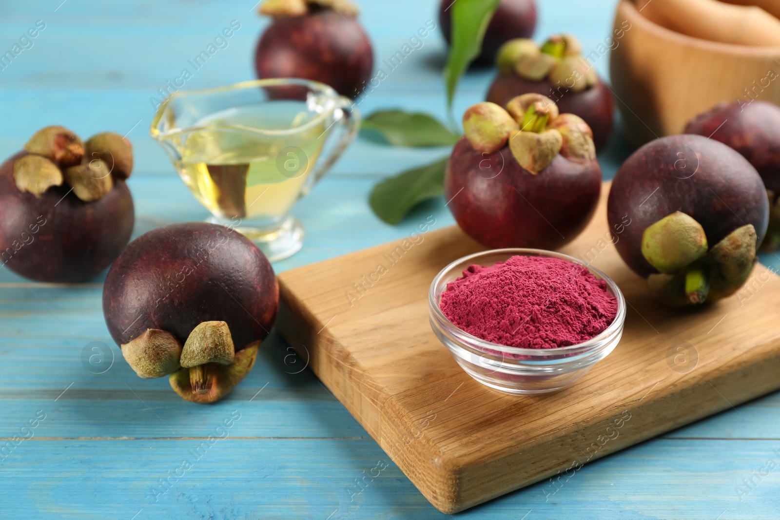 Photo of Purple mangosteen powder and fruits on light blue wooden table