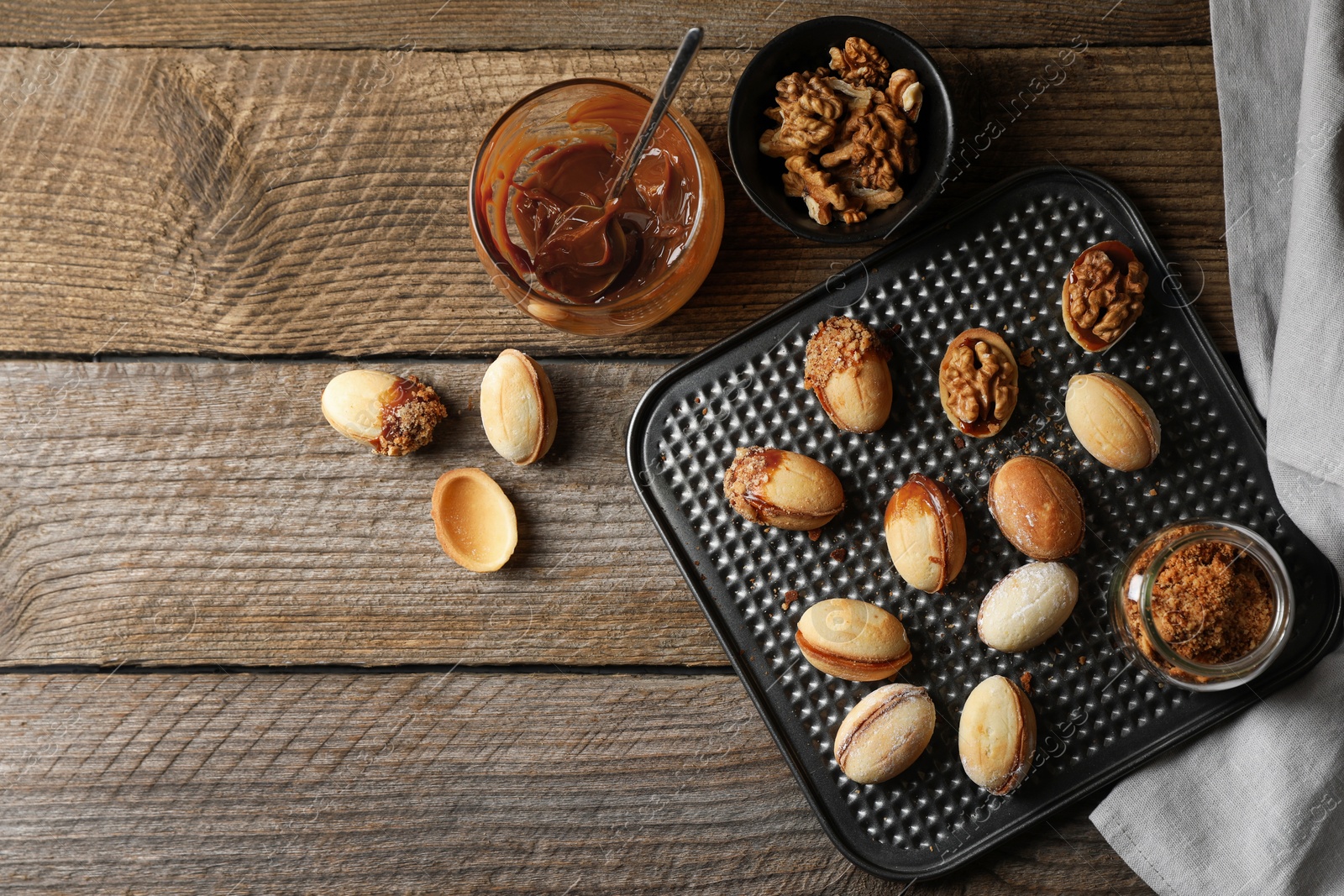 Photo of Freshly baked homemade walnut shaped cookies, boiled condensed milk and nuts on wooden table, flat lay. Space for text