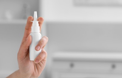 Woman holding nasal spray bottle indoors, closeup. Space for text