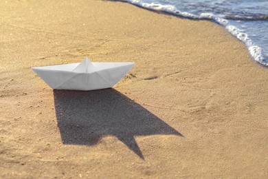 Photo of Beautiful white paper boat on sand near sea, space for text