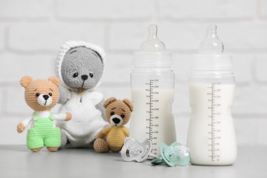 Photo of Feeding bottles with milk, pacifiers and crochet toys on light grey table