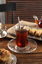 Photo of Traditional Turkish tea in glass and fresh baklava on wooden table