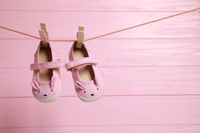 Photo of Cute baby shoes drying on washing line against pink wooden wall. Space for text