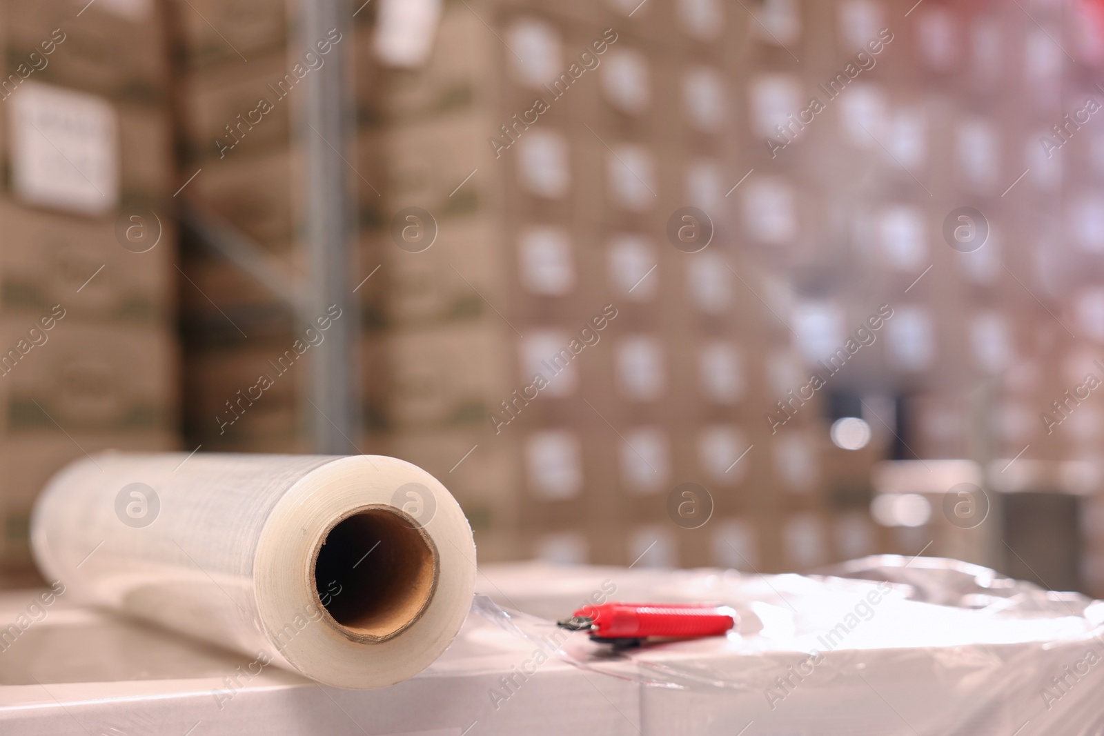 Photo of Roll of stretch film and utility knife on wrapped boxes in warehouse