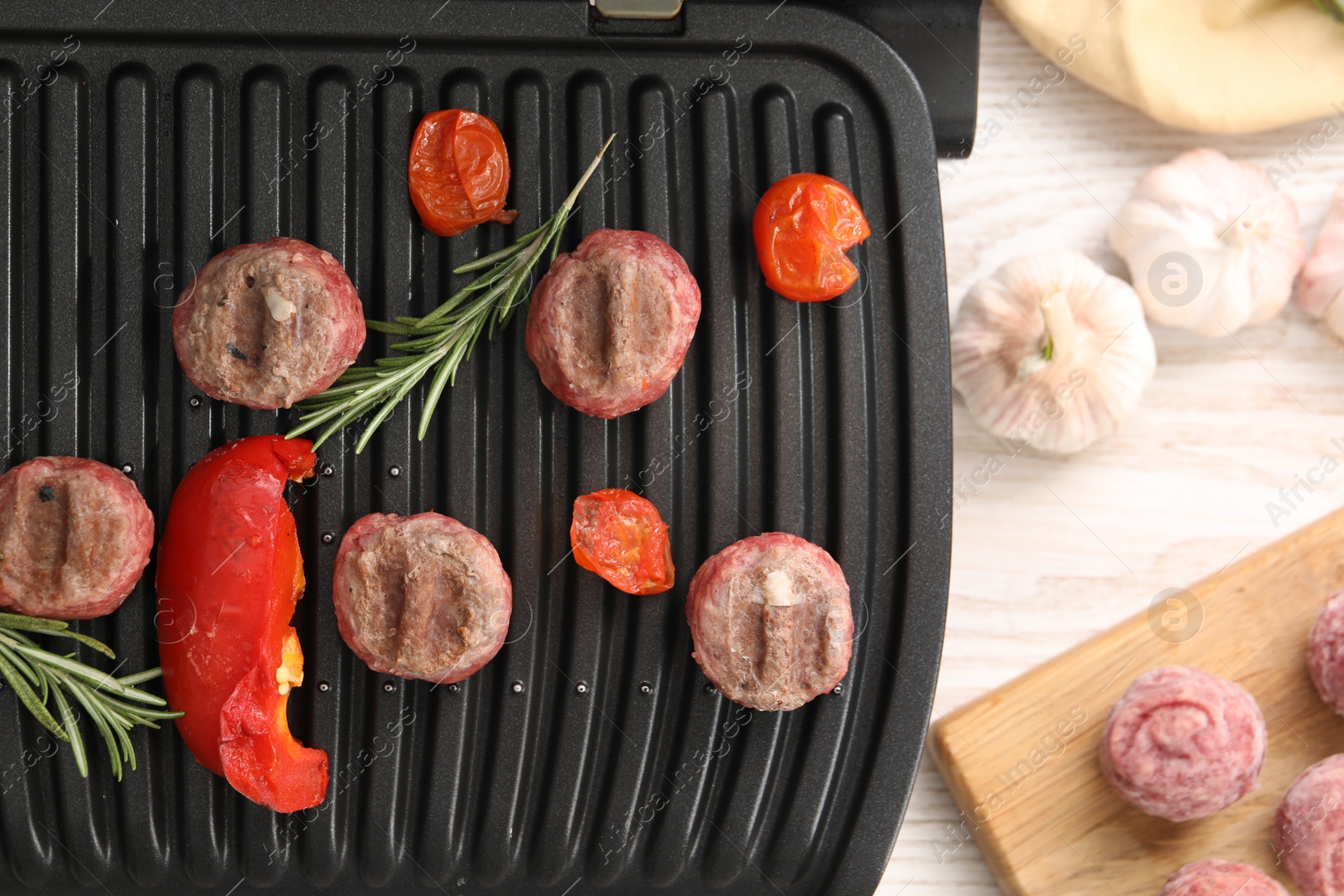 Photo of Electric grill with vegetables, meat balls and rosemary on wooden table, flat lay