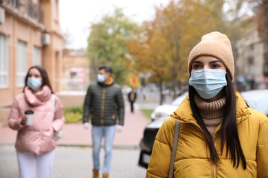 Photo of Young woman in medical face mask walking outdoors. Personal protection during COVID-19 pandemic