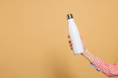 Photo of Woman holding thermos bottle on beige background, closeup. Space for text