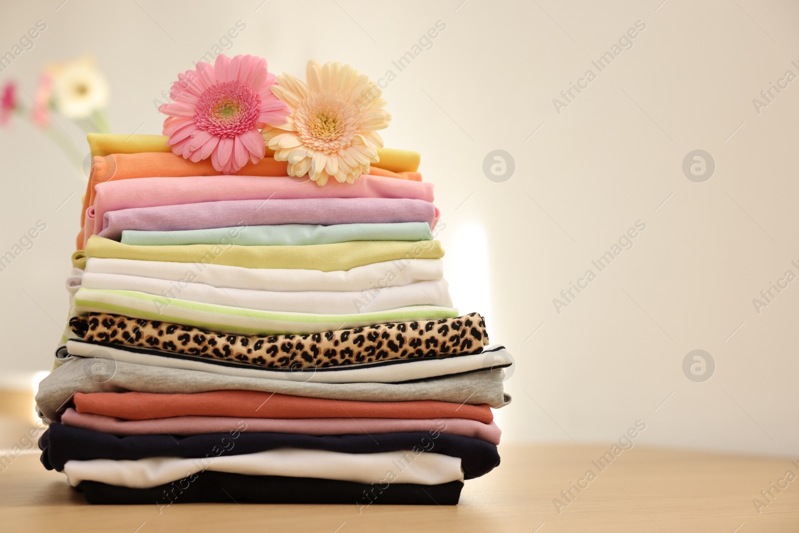 Photo of Stack of clean clothes and flowers on wooden table. Space for text