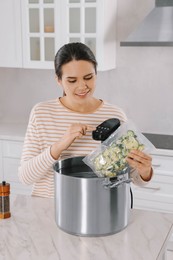 Woman putting vacuum packed broccoli into pot and using thermal immersion circulator. Sous vide cooking