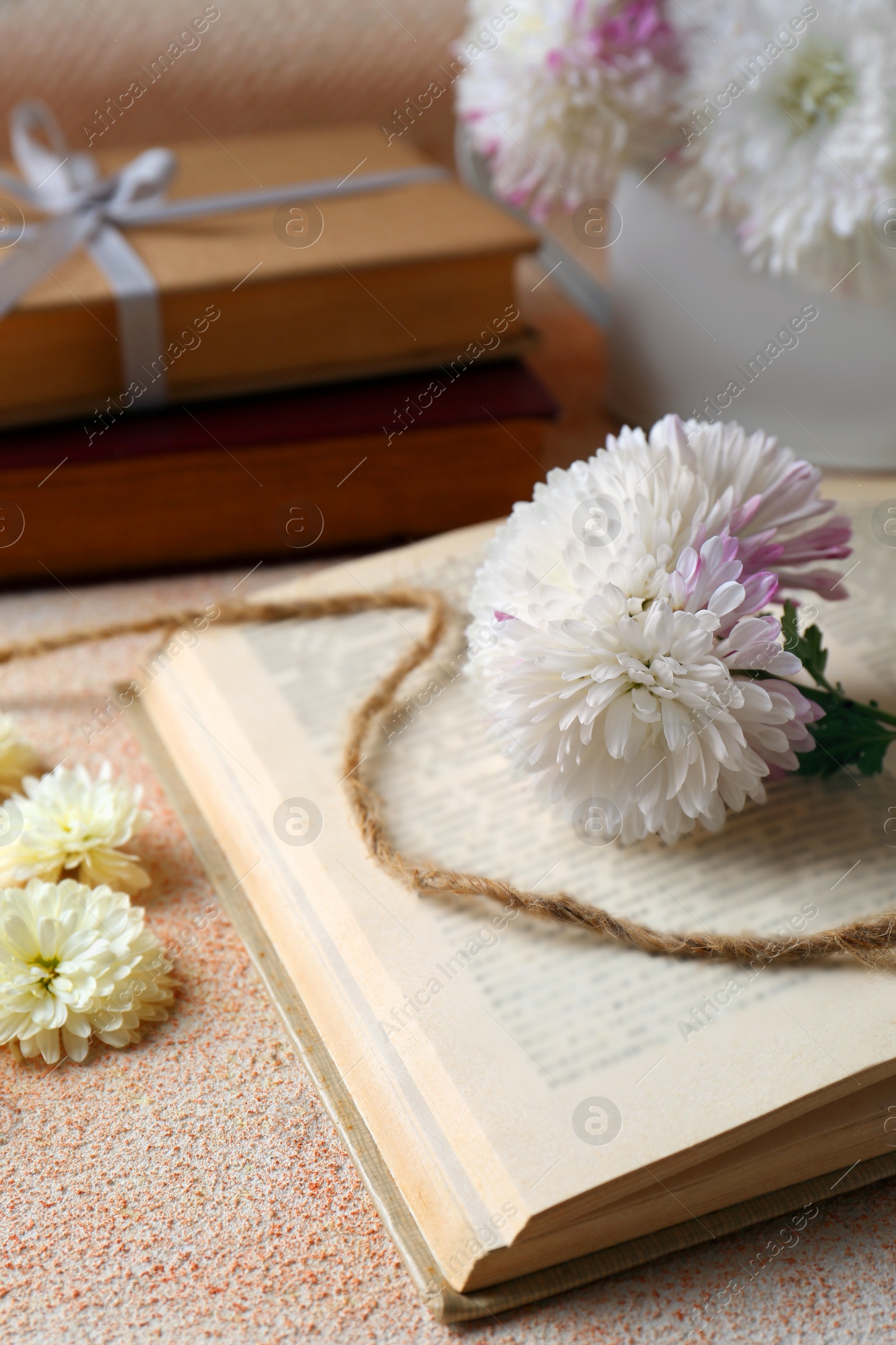 Photo of Book with chrysanthemum flowers as bookmark on beige textured table, closeup