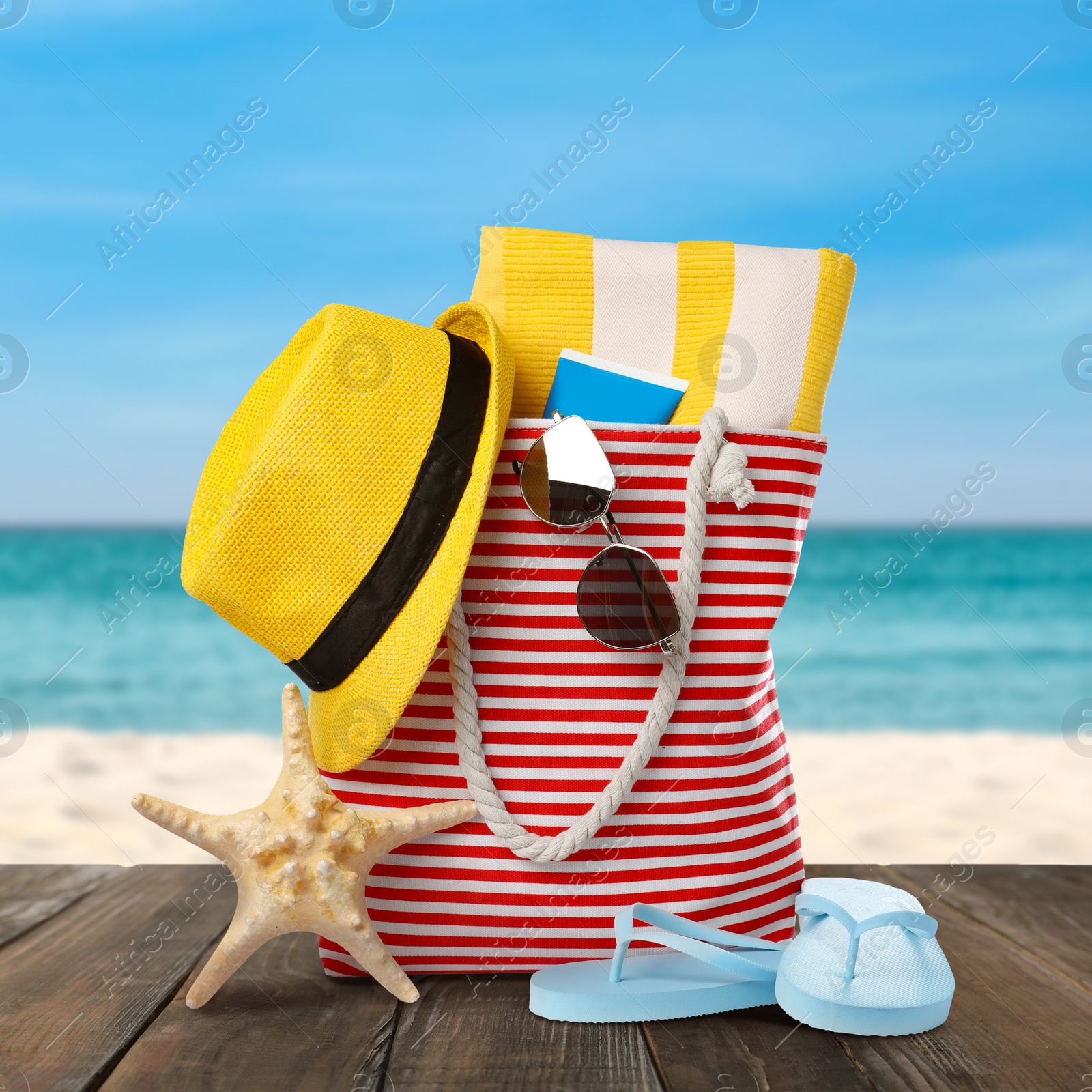 Image of Stylish bag with beach accessories on wooden surface near seashore 