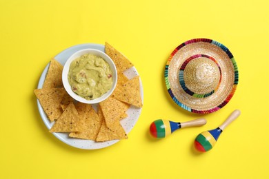 Photo of Mexican sombrero hat, nachos chips, guacamole and maracas on yellow background, flat lay