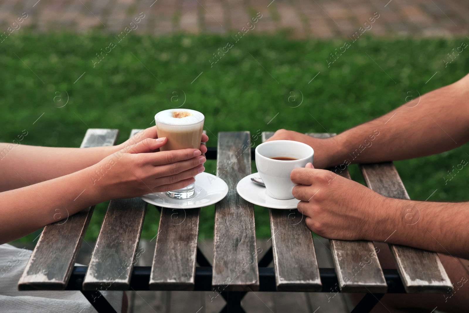 Photo of Man and woman drinking coffee at wooden table in outdoor cafe, closeup