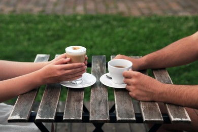 Photo of Man and woman drinking coffee at wooden table in outdoor cafe, closeup