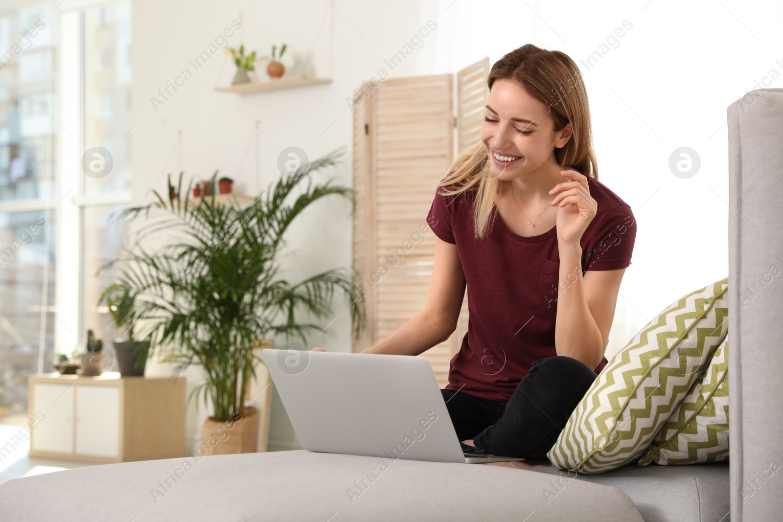 Photo of Young woman using laptop at home, space for text. Trendy room interior with plants