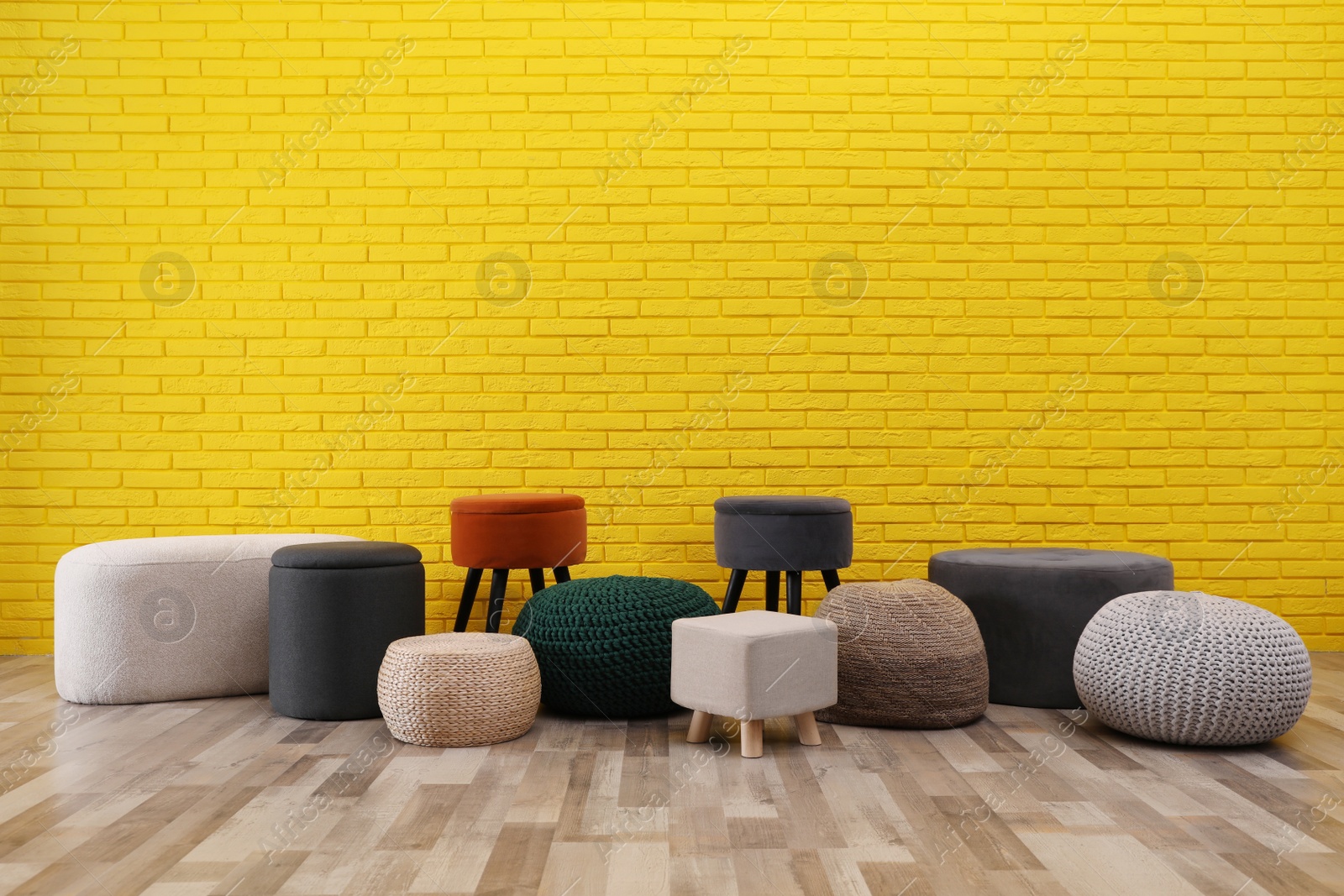 Photo of Different stylish poufs and ottomans near yellow brick wall, space for text