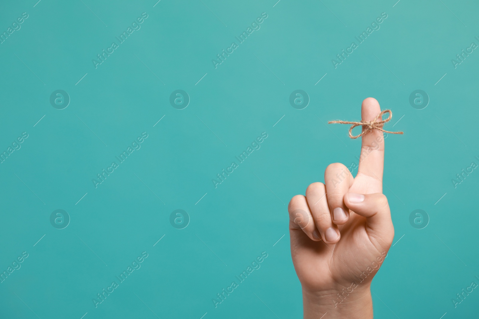 Photo of Man showing index finger with tied bow as reminder on turquoise background, closeup. Space for text