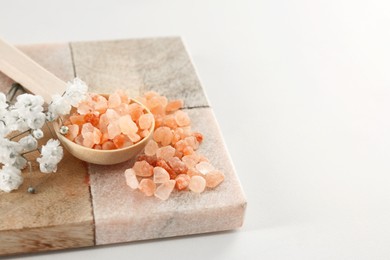 Photo of Orange sea salt and beautiful flowers on white table, closeup. Space for text