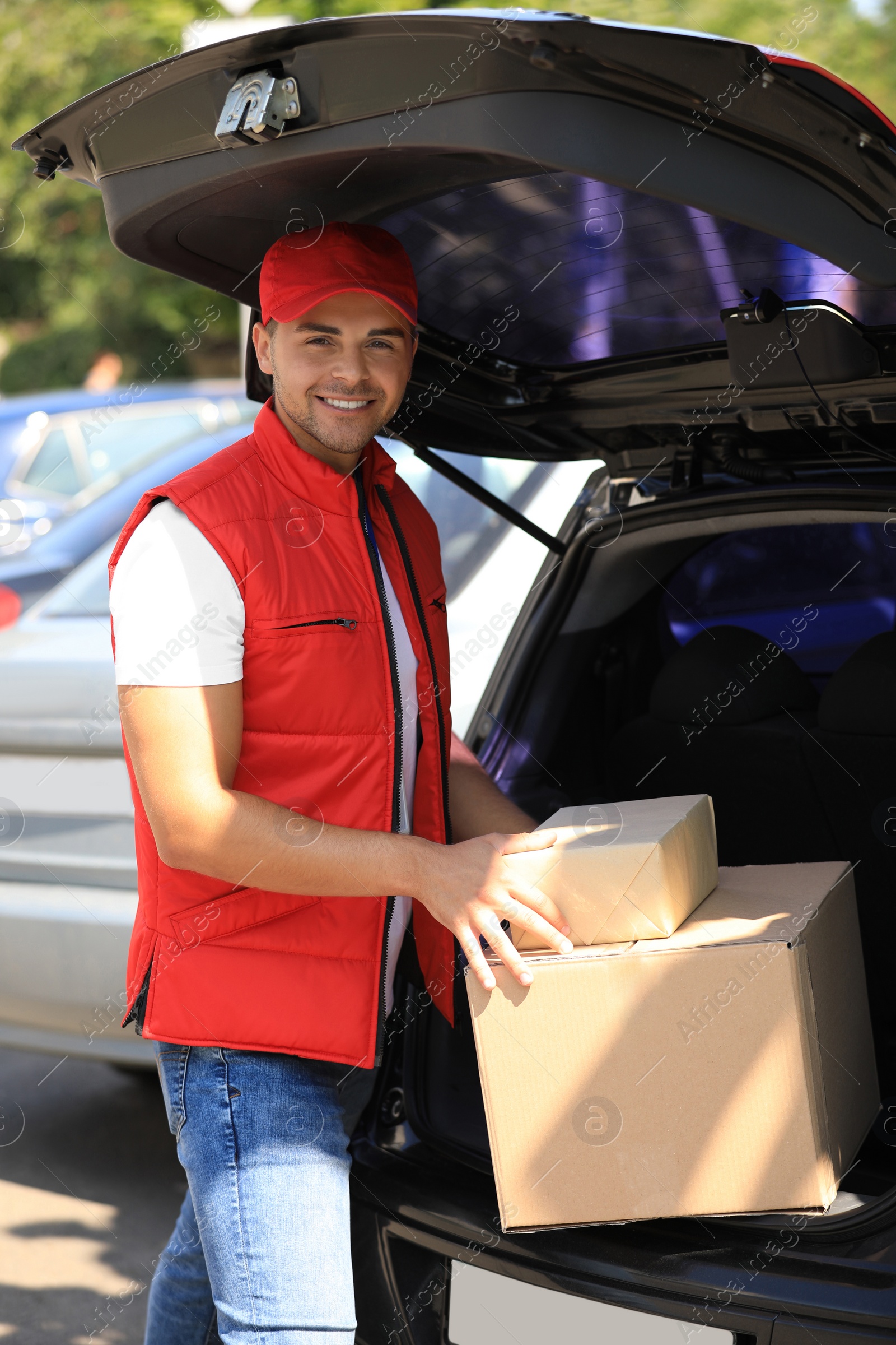 Photo of Young courier holding parcels near delivery car outdoors