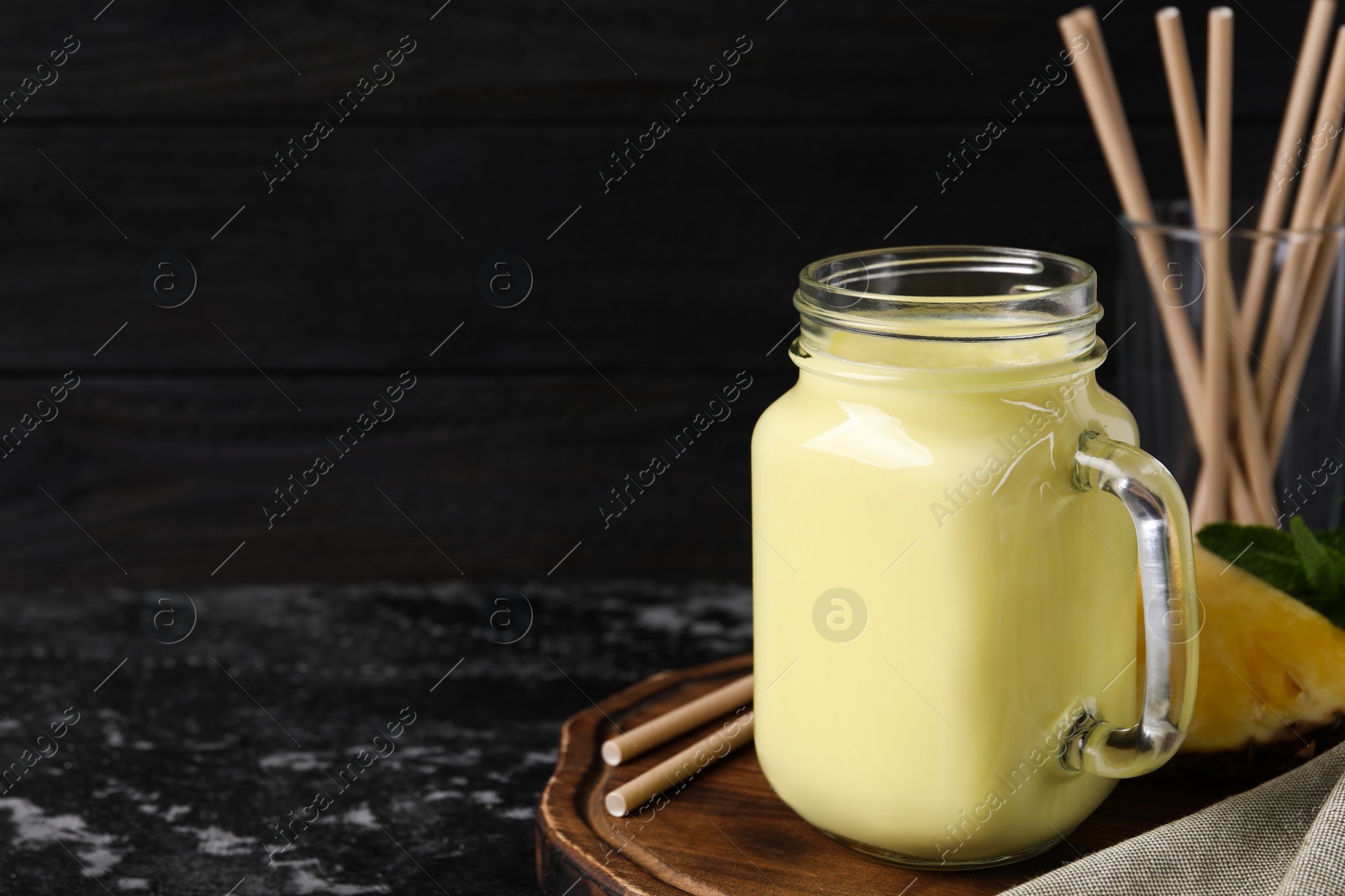Photo of Tasty pineapple smoothie, slice of fruit and straws on dark textured table. Space for text