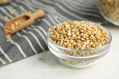 Photo of Uncooked green buckwheat grains in bowl on white wooden table