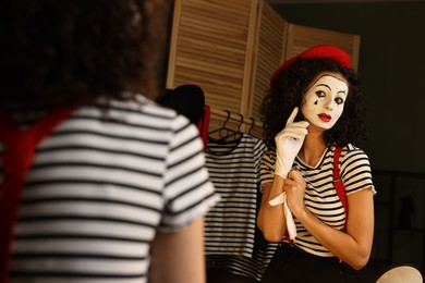 Young woman in mime costume putting gloves near mirror indoors