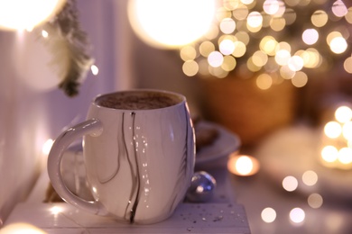 Photo of Cup of tasty hot drink against blurred Christmas lights. Space for text