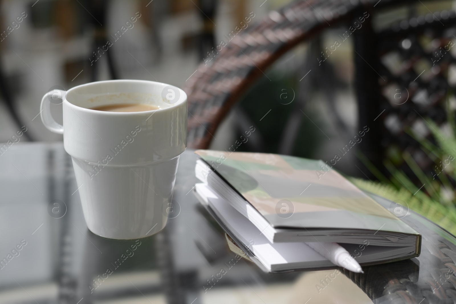 Photo of Ceramic cup of drink and notebook with pen on glass table outdoors. Good morning