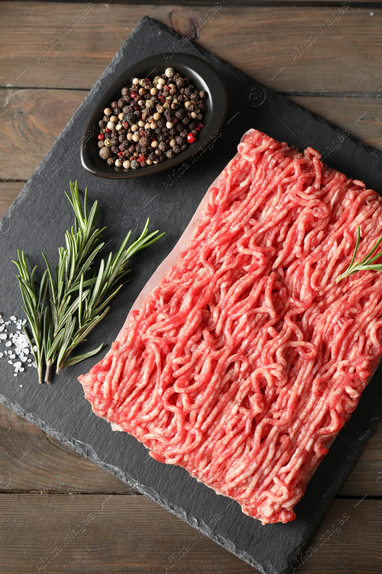 Photo of Raw ground meat, spices and rosemary on wooden table, top view