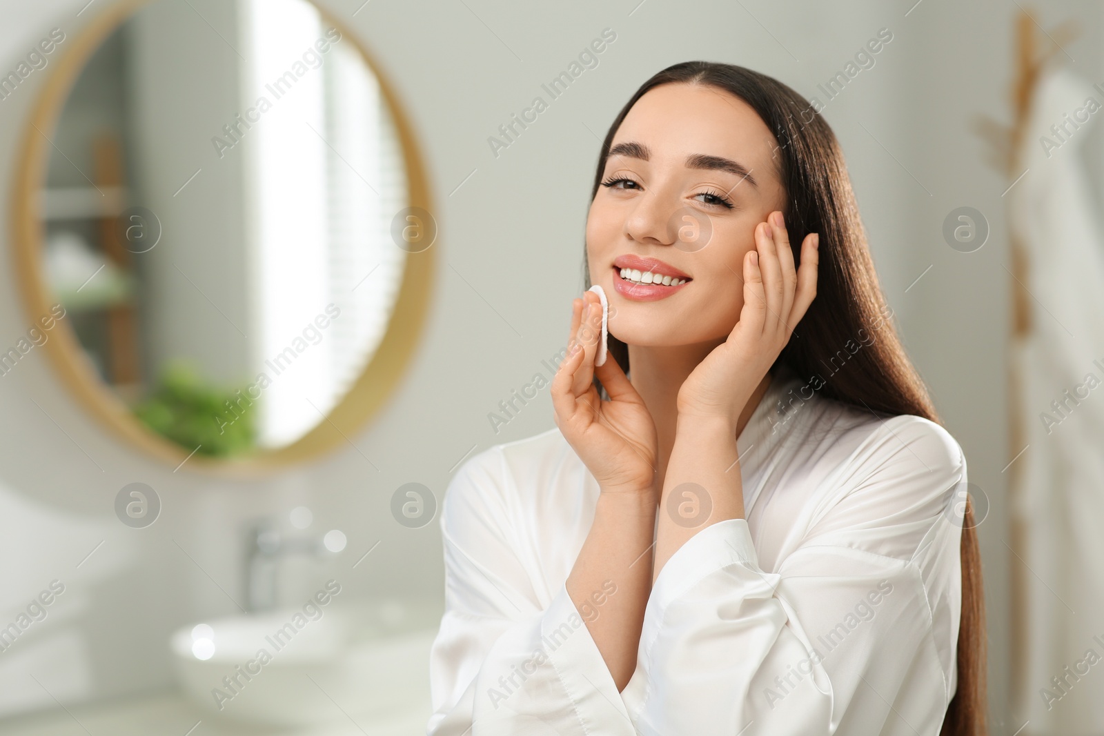 Photo of Beautiful woman removing makeup with cotton pad indoors