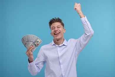 Happy man with dollar banknotes on light blue background