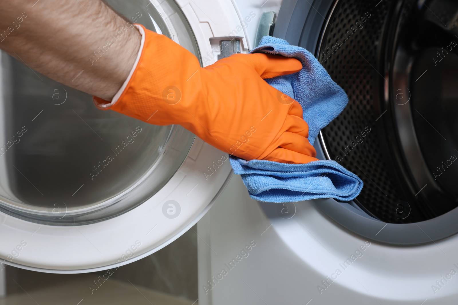 Photo of Man cleaning empty washing machine with rag, closeup